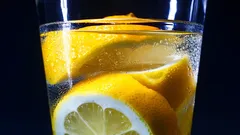Sklenice vody s plátky citronu a bublinkami na tmavém pozadí