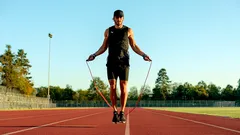 Muž skáče přes švihadlo na atletické dráze za slunečného dne