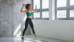 Žena skáče při domácím kardio cvičení ve světlém pokoji u okna.