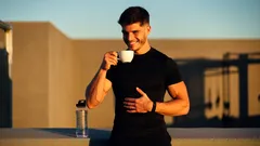 Muž ve sportovním oblečení pije kávu venku za ranního slunce