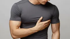 Muž držící se za hruď, bolest v oblasti hrudi, šedé tričko, zdravotní potíže